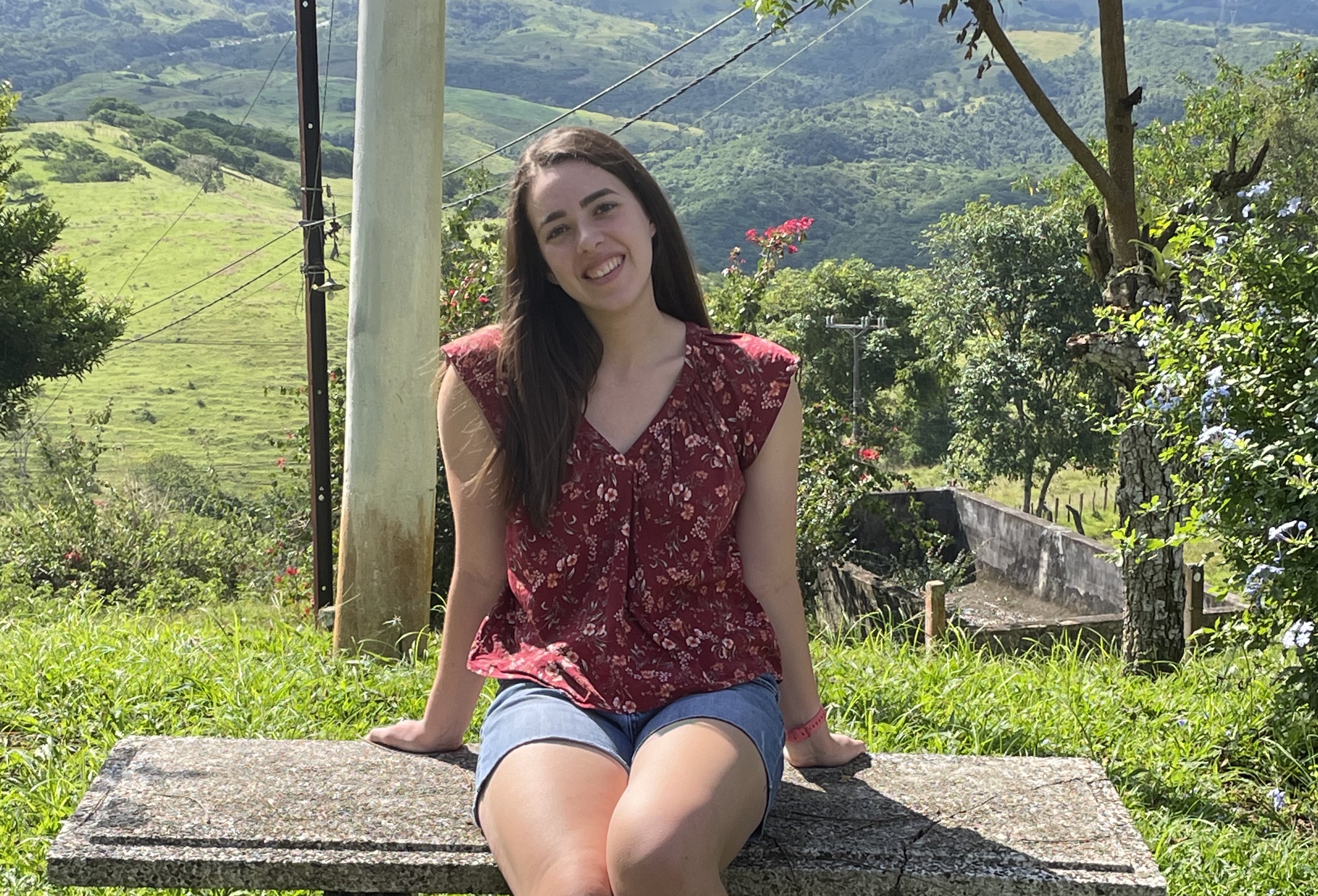 Julia Rossigno sits on a bench overlooking a vast green landscape. 