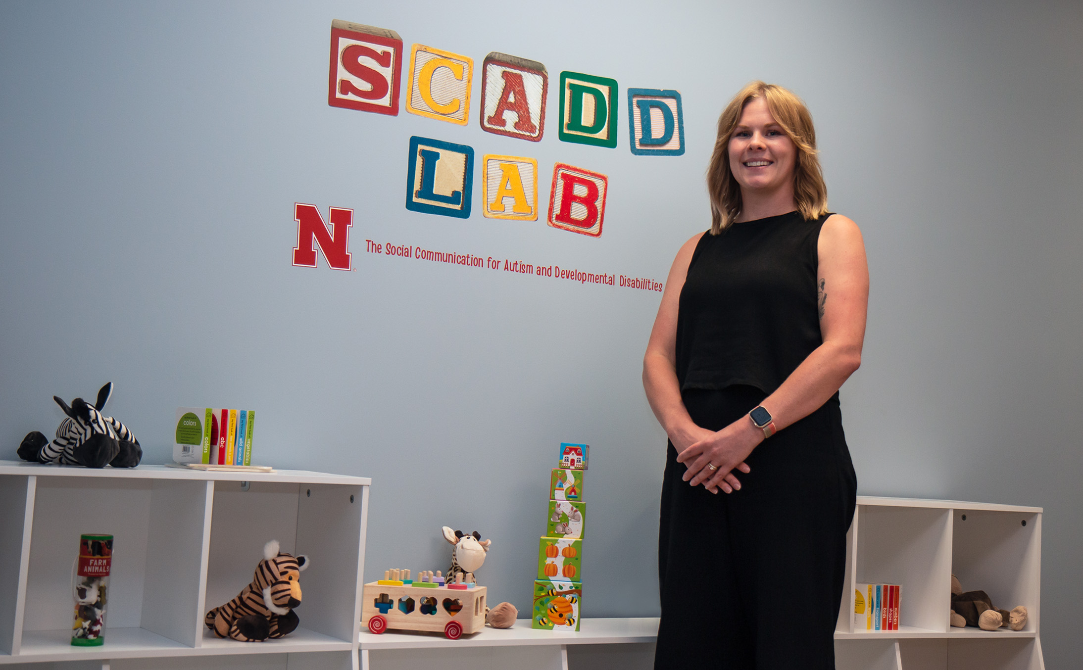 Ciara Ousley stands in front of a blue wall with colorful blocks that spell out SCADD LAB. 