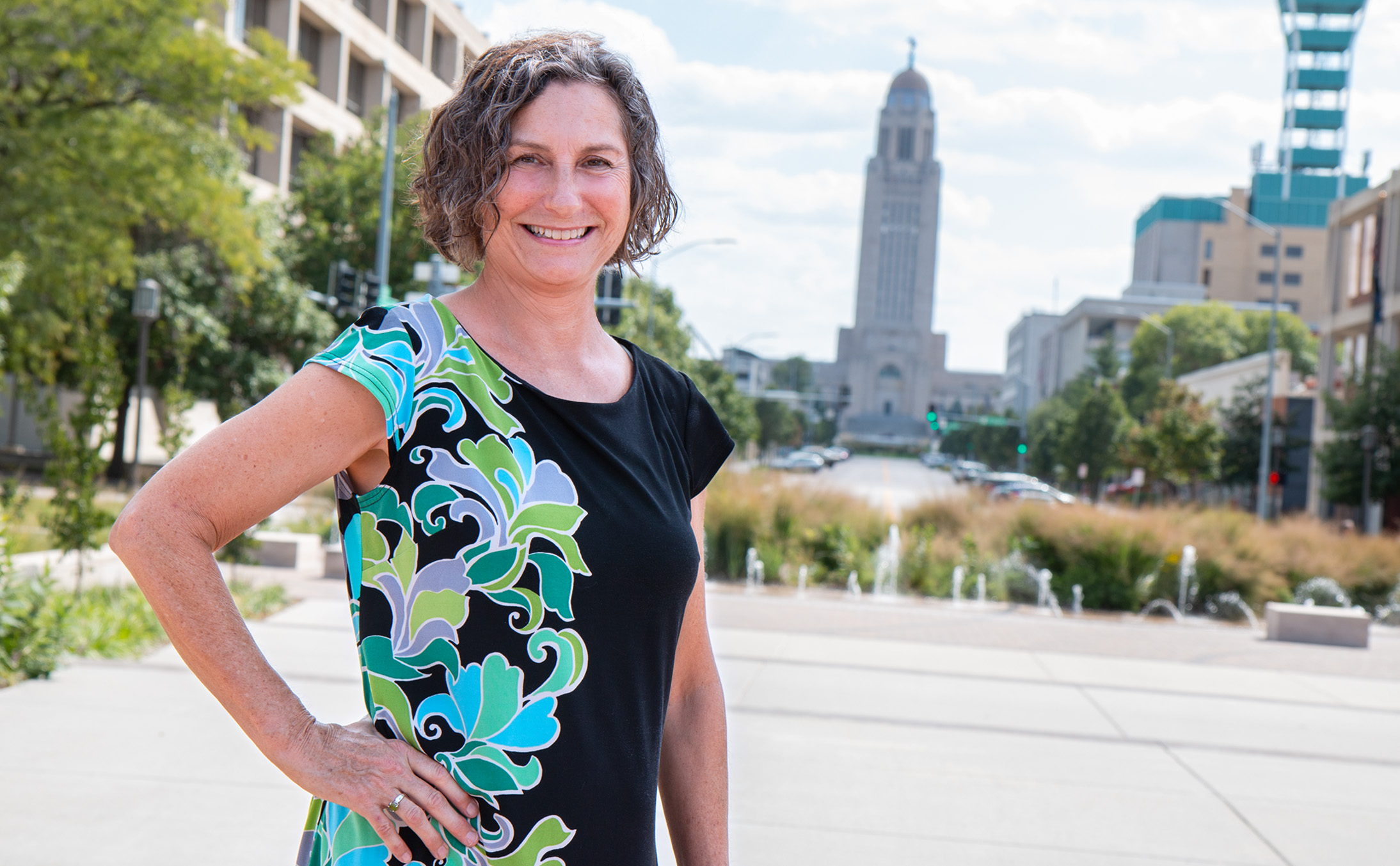 Julia Torquati stands smiling outdoors with the Nebraska State Capitol behind her. 