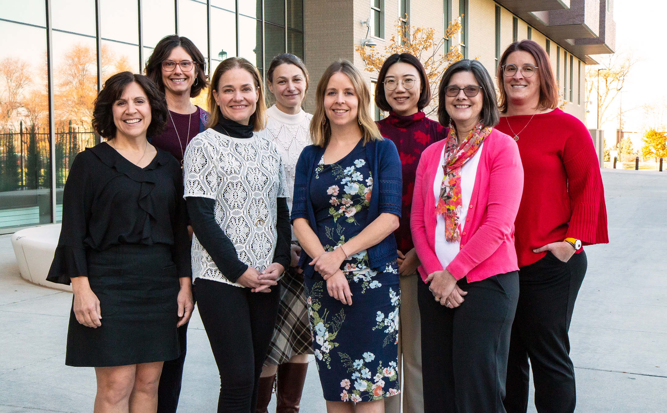 Eight individuals dressed in business clothing stand outdoors smiling for a photo. 