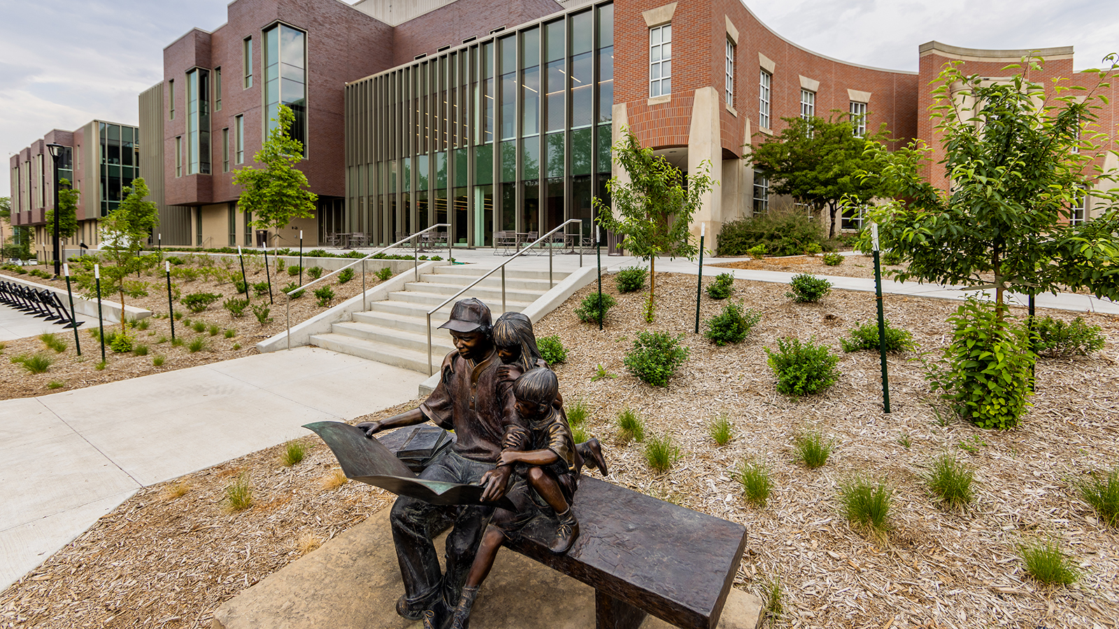 a sculpture of a man reading to a child on a bench outside Teachers College Hall with Carolyn Pope Edwards Hall in the background