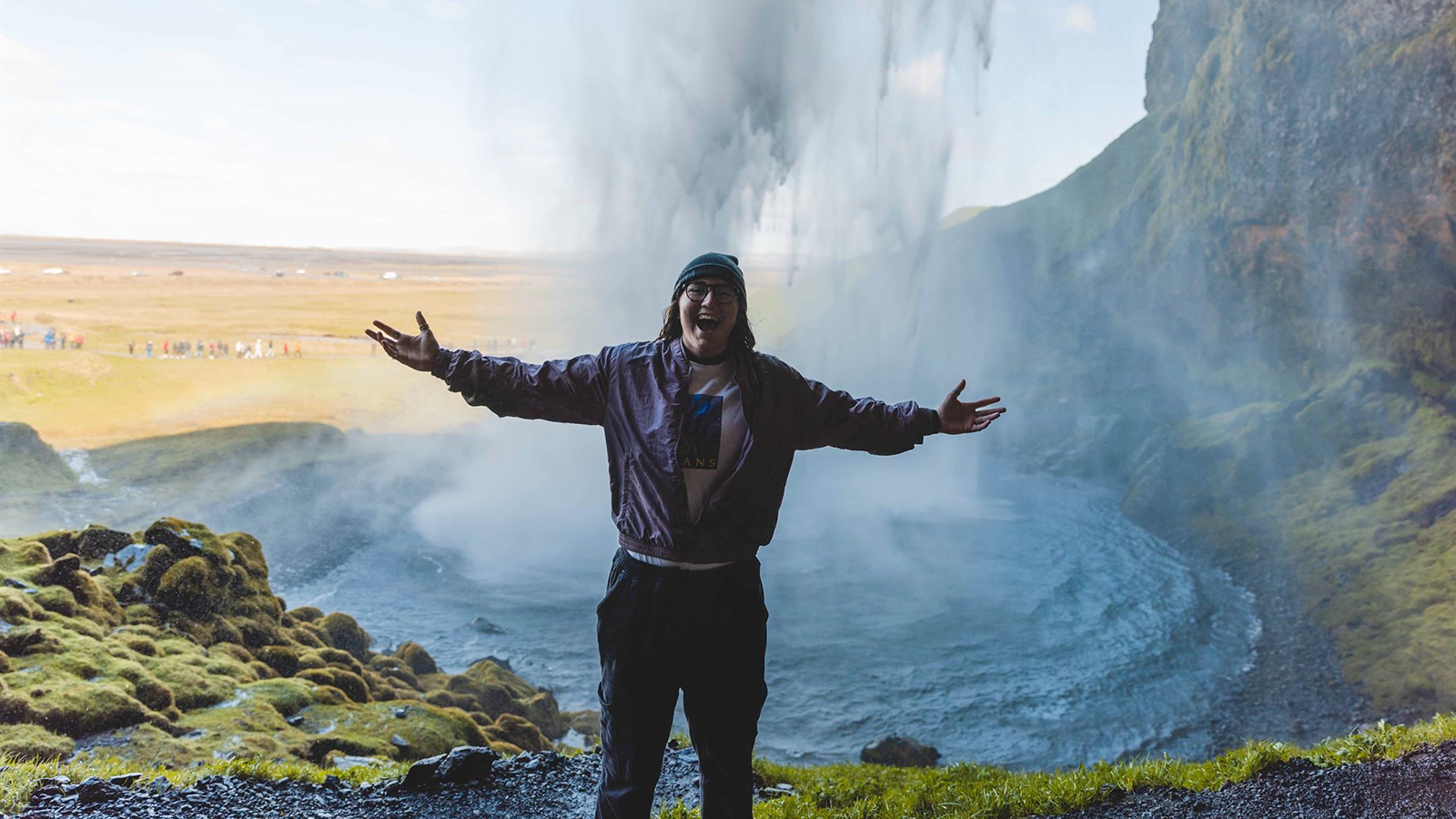 Cece Villa stands with arms open in front of a waterfall