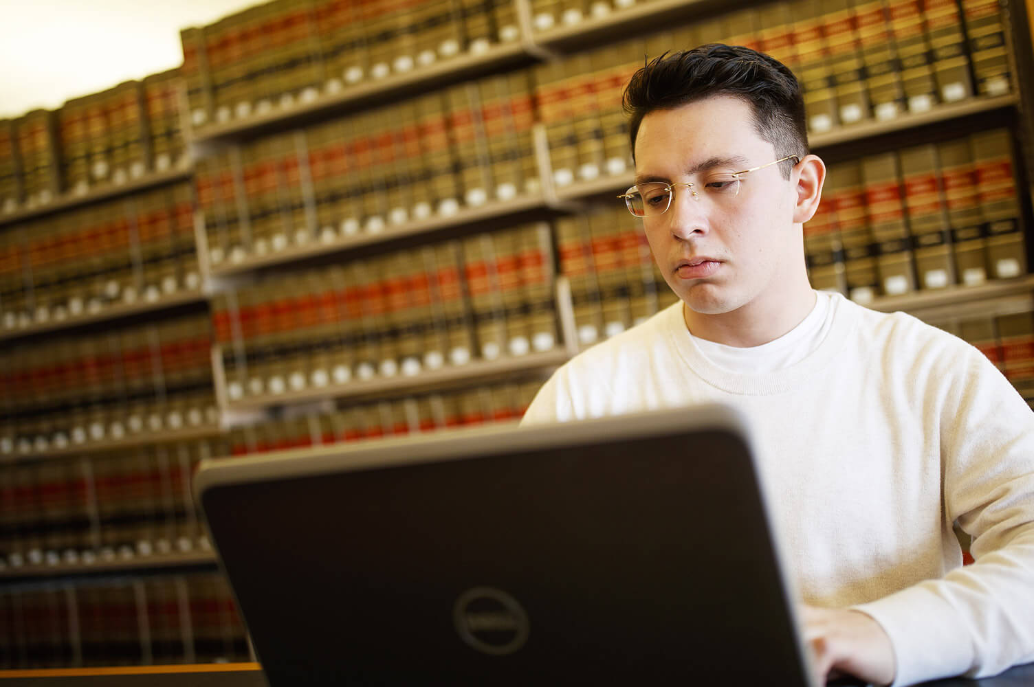 Student working on laptop in front of large bookshelf