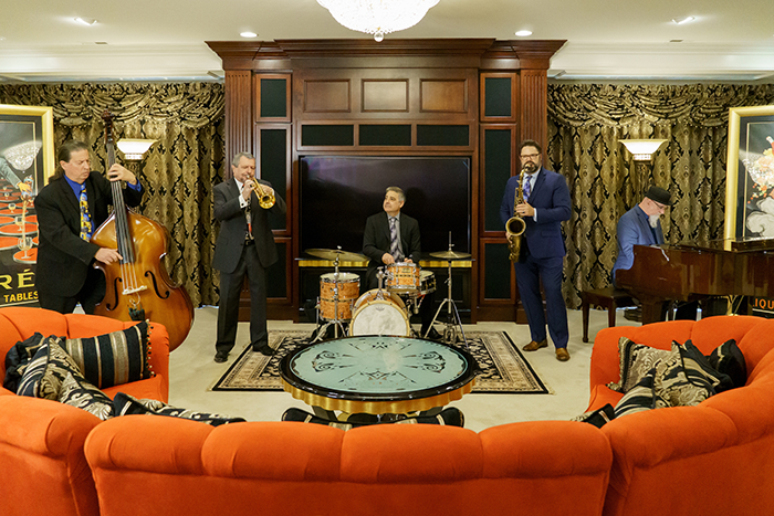 The Metro Jazz Group wearing black suits playing in a living room setting with a large orange couch in the foreground