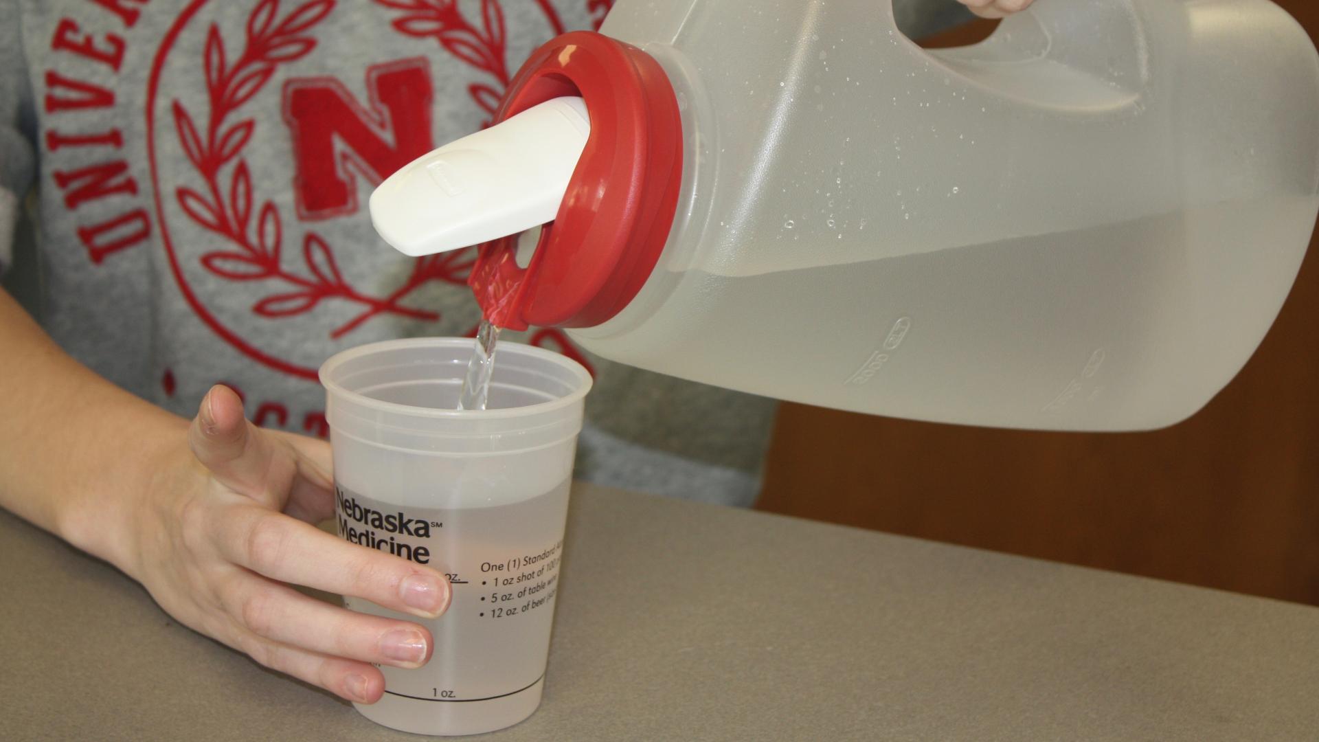 Student pours water into a cup with ounce markings to determine how much is in a standard alcoholic beverage.